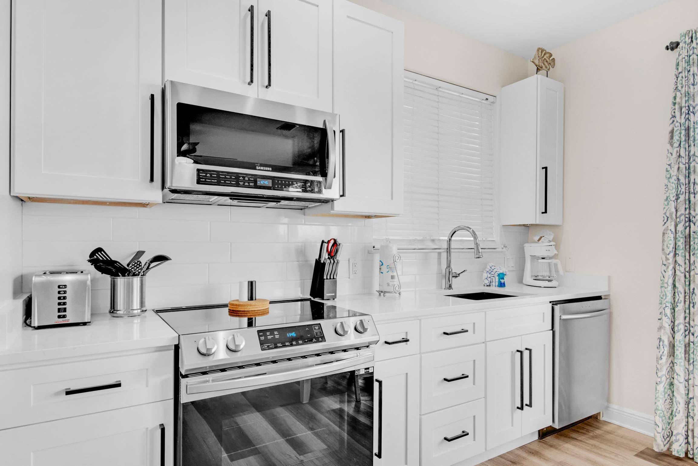 Una cocina moderna con armarios blancos, un microondas de acero inoxidable, una estufa a gas, un horno empotrado y un fregadero.