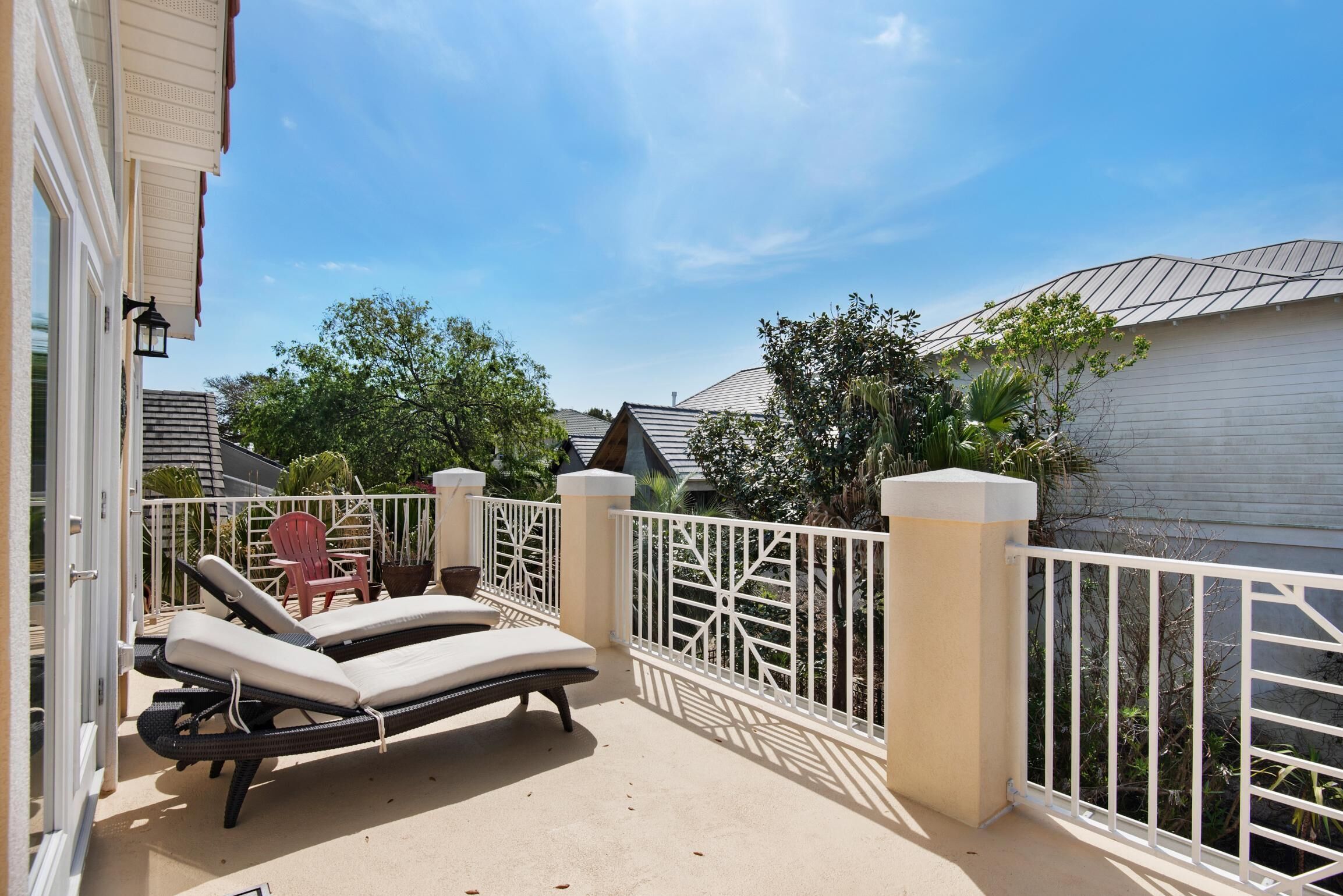 A balcony with two lounge chairs, a white fence, and a view of neighboring houses.