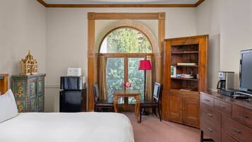 Une chambre d’hôtel comprenant un lit, un bureau avec un ordinateur, une télévision, une armoire et une fenêtre donnant sur des arbres.