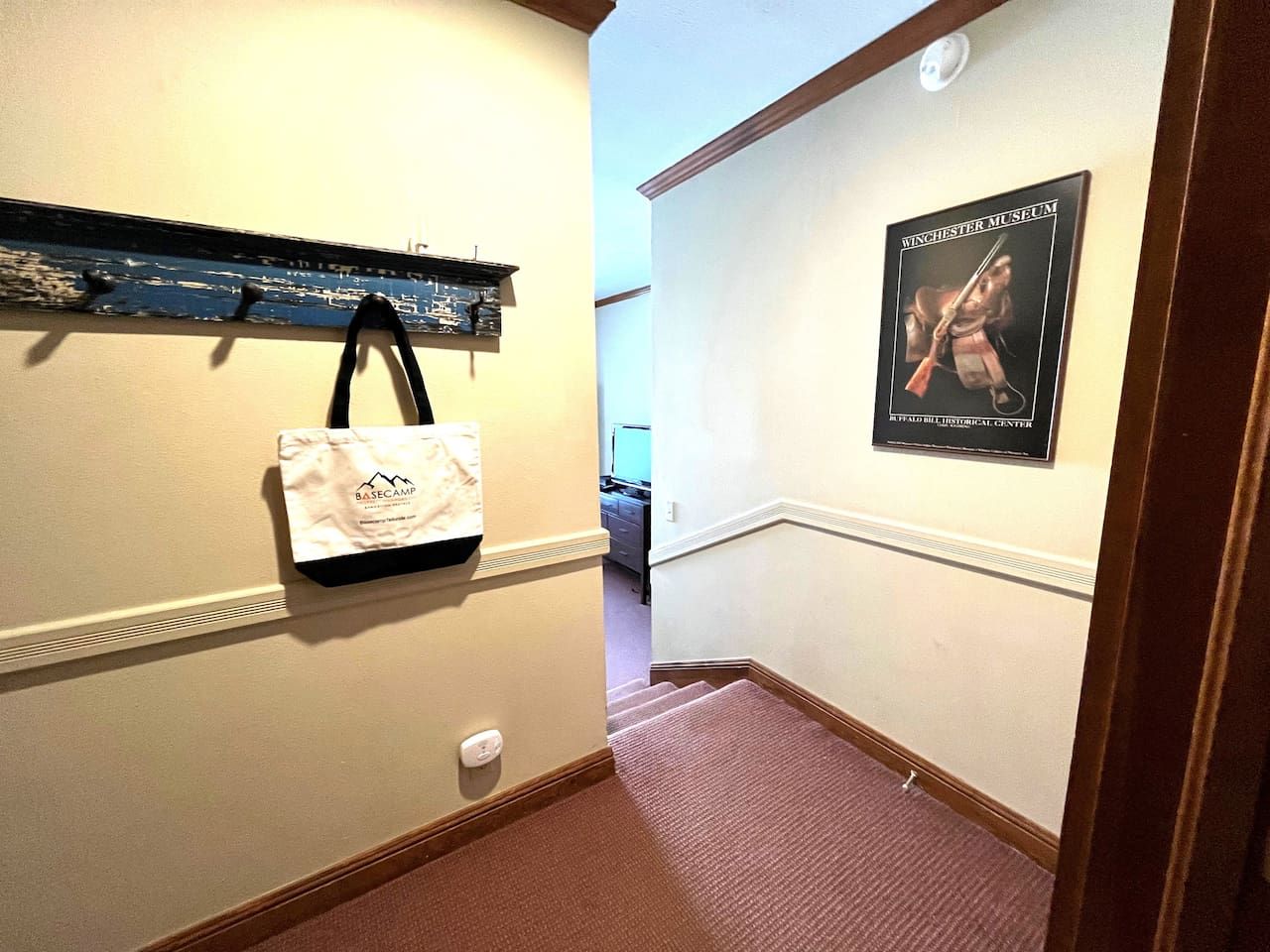Un couloir avec un mur blanc, un tableau encadré représentant une figure historique et un sac blanc accroché au mur.