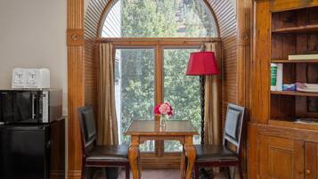 Une pièce avec une table en bois et deux chaises, une lampe rouge, un réfrigérateur et une fenêtre donnant sur des arbres.