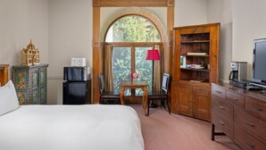 A hotel room with a large bed, a desk with a computer, a television, and a wooden cabinet.