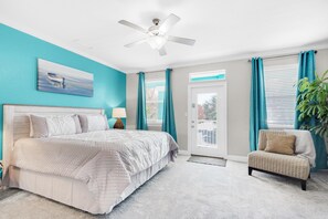 Une chambre à coucher avec un lit, une chaise, un ventilateur de plafond et une fenêtre avec des rideaux.