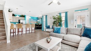 A modern living room with a sofa, coffee table, and a dining area with chairs and a kitchen in the background. - Turquoise Waters (Destin)