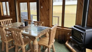 L’intérieur d’un chalet en bois comprend une table à manger avec un plateau en verre, des chaises en bois, une cheminée et de grandes fenêtres.