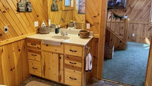 Une salle de bain rustique, avec une cabine en bois, un lavabo, un miroir et des armoires en bois.