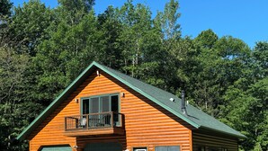 Une cabane en rondins avec un toit végétalisé, une véranda et un garage.
