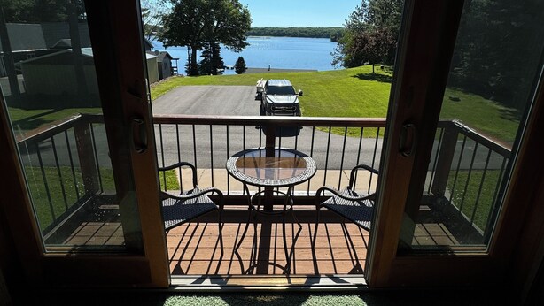 Vue depuis une pièce dont la porte est en verre, donnant sur une terrasse, avec vue sur un lac et un véhicule garé.