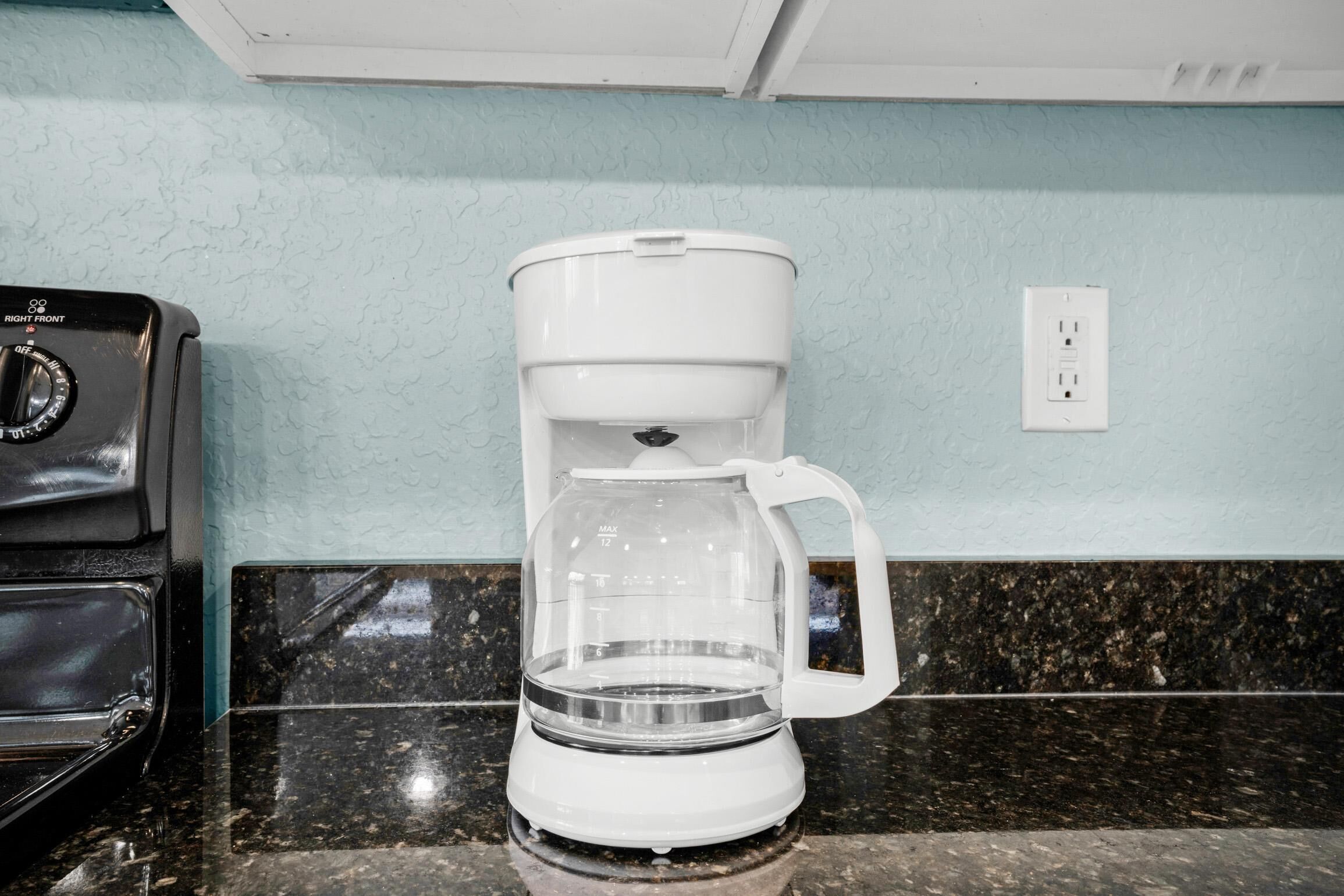 Una cocina con una cafetera sobre la encimera, una estufa y un enchufe en la pared.