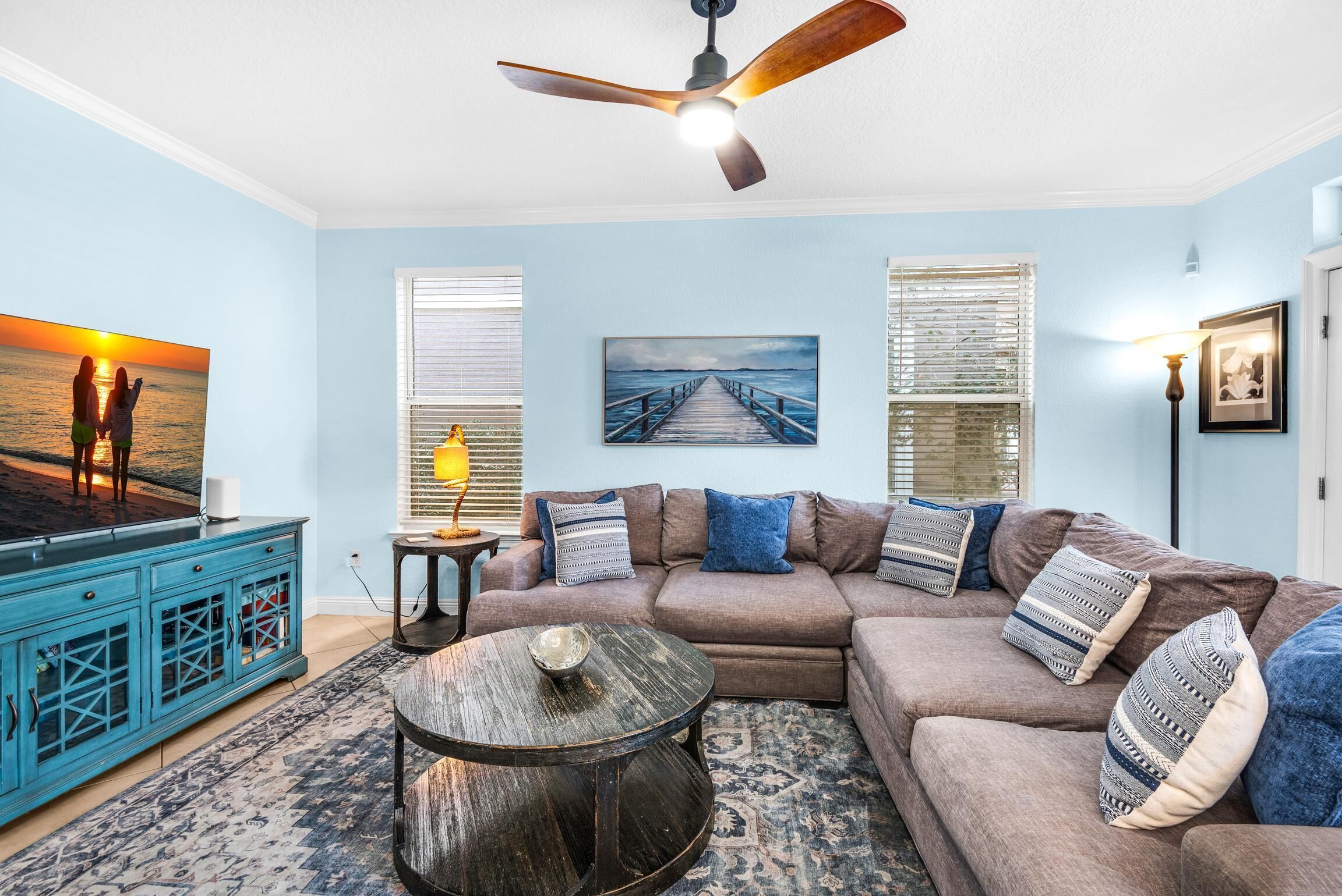 A living room with a sectional sofa, a coffee table, a ceiling fan, and artwork on the walls.