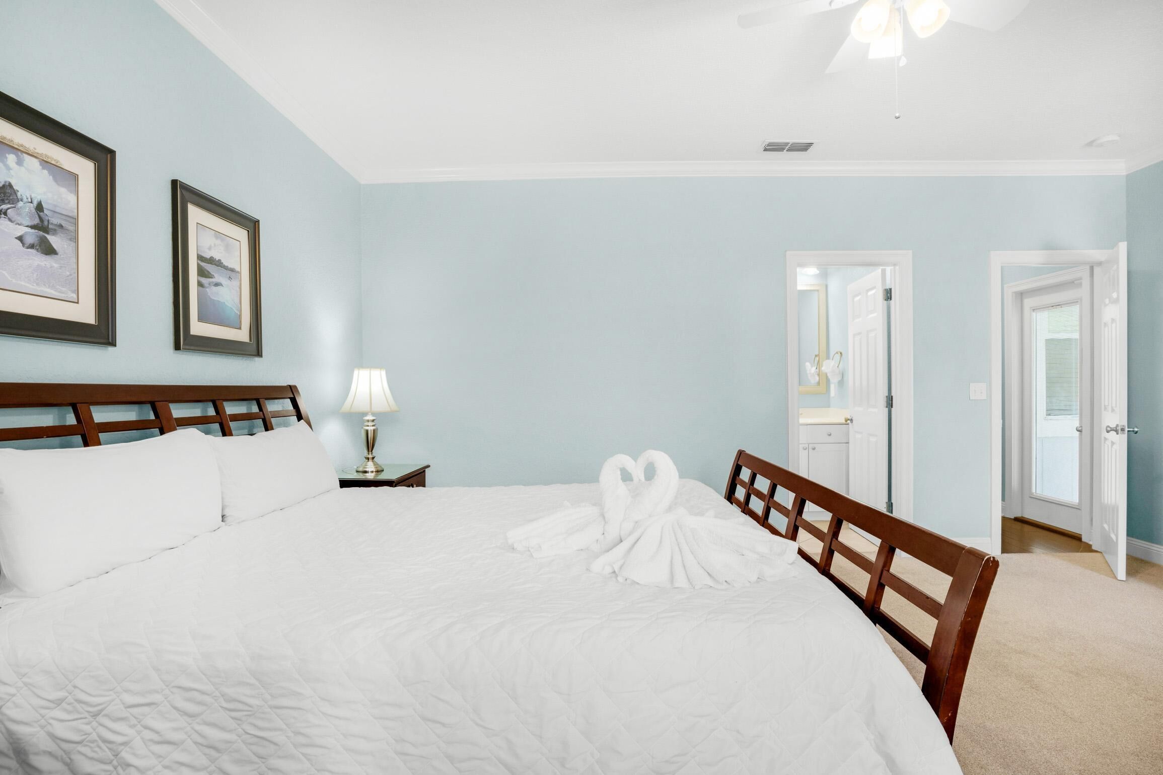 A neatly made bed with a white comforter and pillows, a wooden headboard, a bedside lamp, and two framed pictures on the wall.