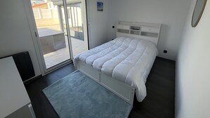 A bedroom with a bed, a sliding glass door to a balcony, and a small bedside table.