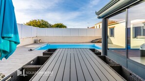 A swimming pool with a wooden deck, a covered area with a blue canopy, and a white fence.