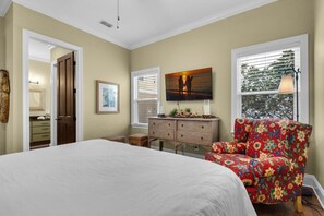 A bedroom with a large bed, a wooden dresser, a floral armchair, and a painting on the wall. - Happily Ever After (Destin)