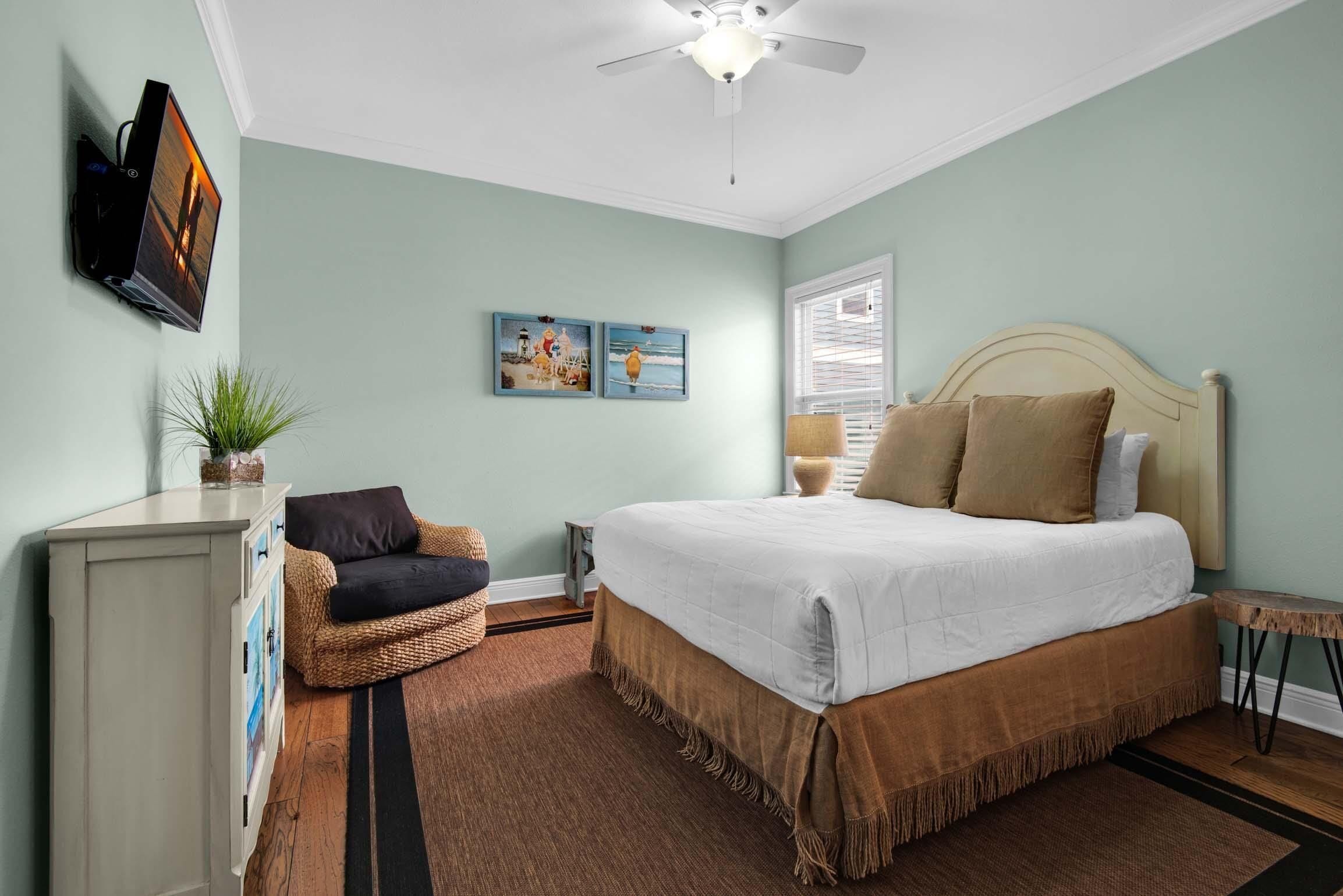 A bedroom with a bed, a dresser, a chair, a ceiling fan, and wall art.