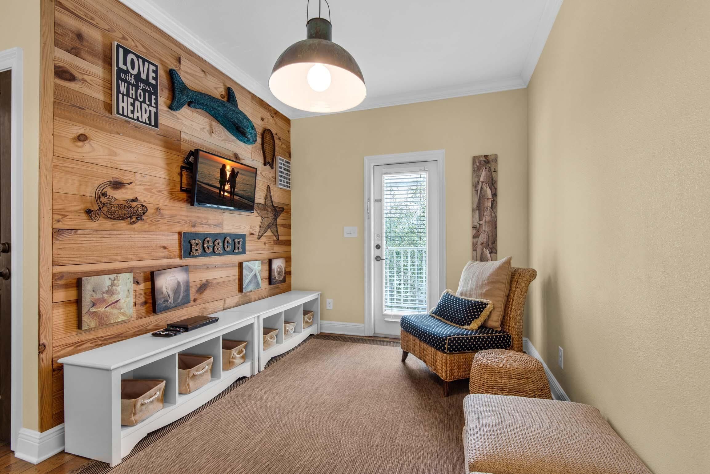 Un hall d’entrée accueillant, avec un mur en bois orné de divers éléments décoratifs, un banc blanc avec espace de rangement et un banc en osier agrémenté de coussins.