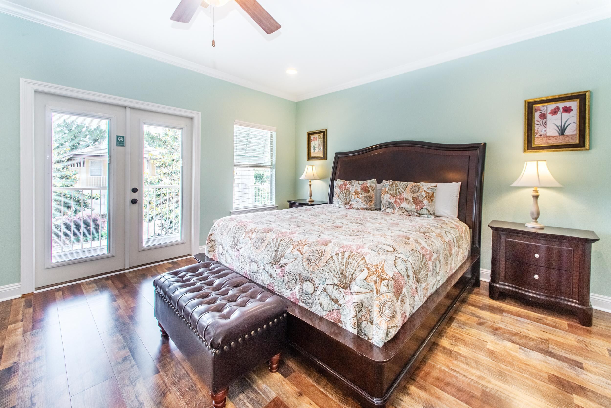 A bedroom with a large bed, a wooden bench, two bedside tables with lamps, and a ceiling fan.