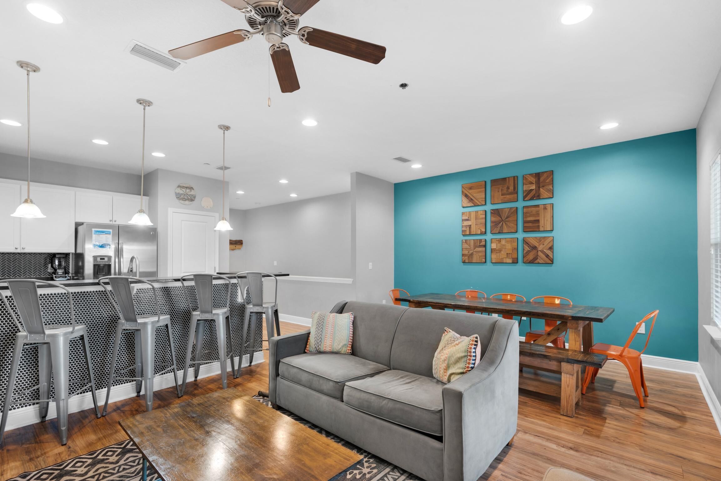 A modern kitchen with white cabinets, a built-in refrigerator, and a dining area with a wooden table and orange chairs.