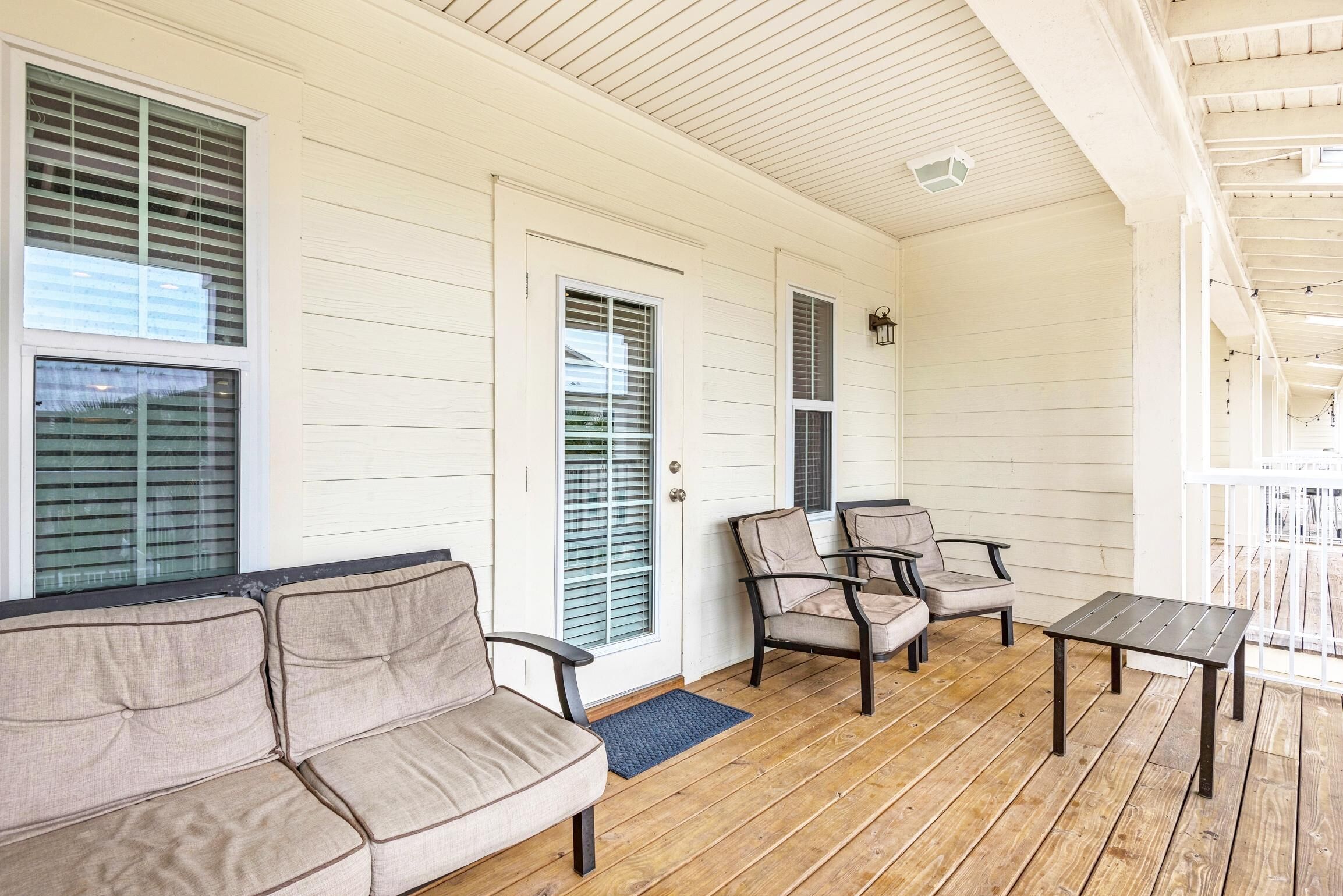 A covered porch with a beige sofa, two armchairs, and a small table.