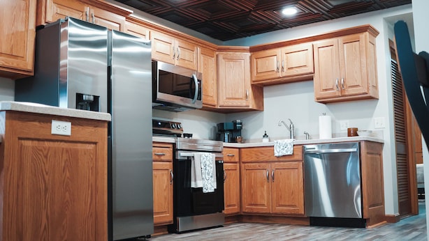 A modern kitchen with wooden cabinets, stainless steel appliances, and a wooden ceiling.