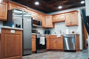 A modern kitchen with wooden cabinets, stainless steel appliances, and a wooden ceiling.