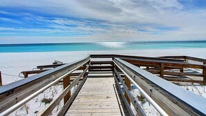 Une promenade en bois qui mène à une plage, avec un ciel dégagé et une mer calme.