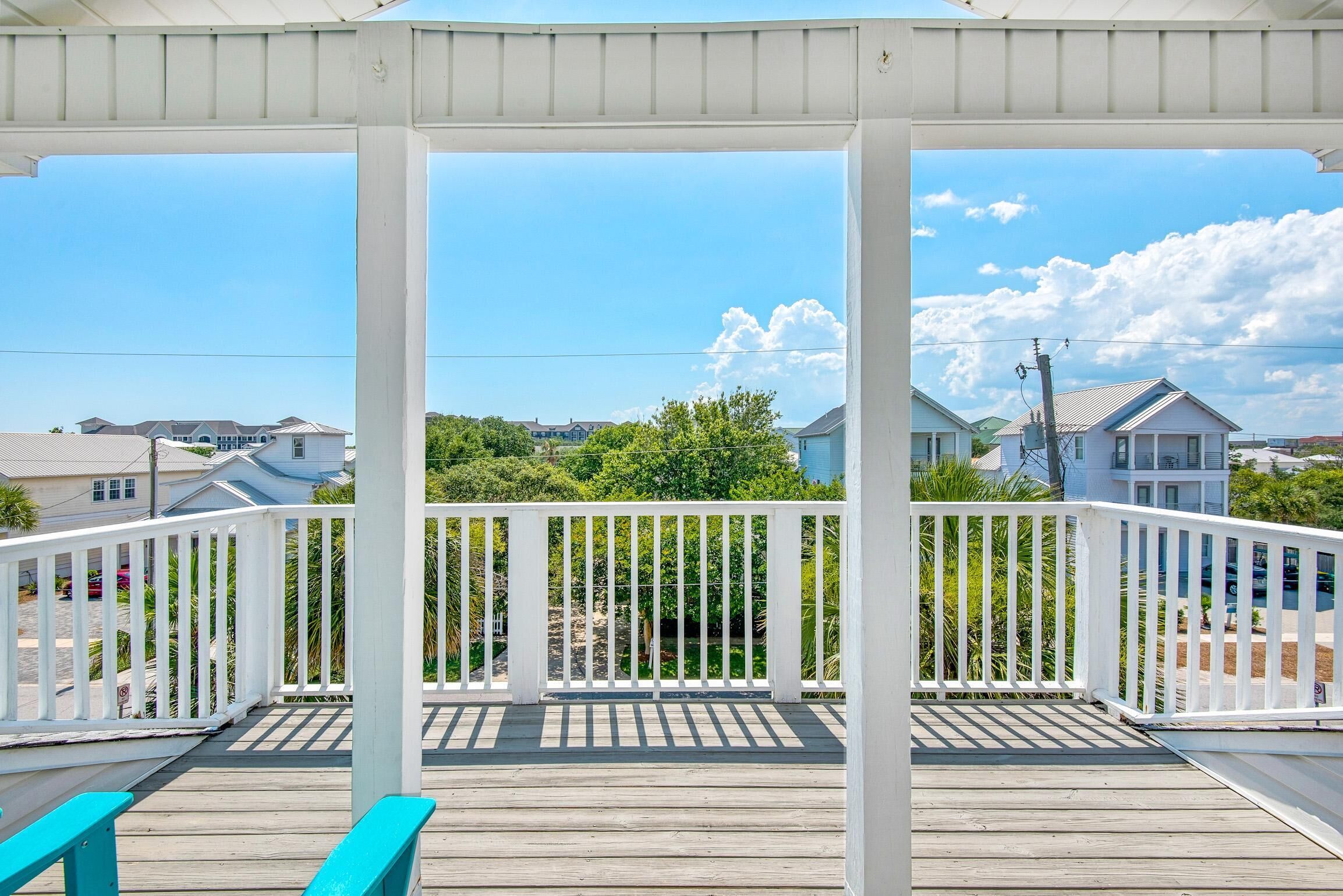 A covered wooden deck with white railings, overlooking a residential area with houses and greenery.