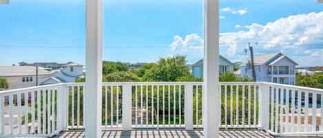 A covered wooden deck with white railings, overlooking a residential area with houses and greenery.