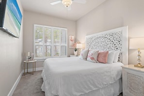 A bedroom with a bed, a nightstand, a lamp, a window with blinds, and a ceiling fan. - Seahaus (Destin)