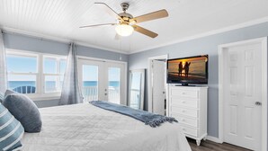 A bedroom with a bed, a ceiling fan, a TV, and a view of the ocean. - Pointe of View (Destin)
