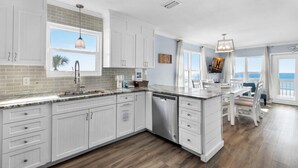 A modern kitchen with white cabinetry, a large island, and a view of the ocean. - Pointe of View (Destin)