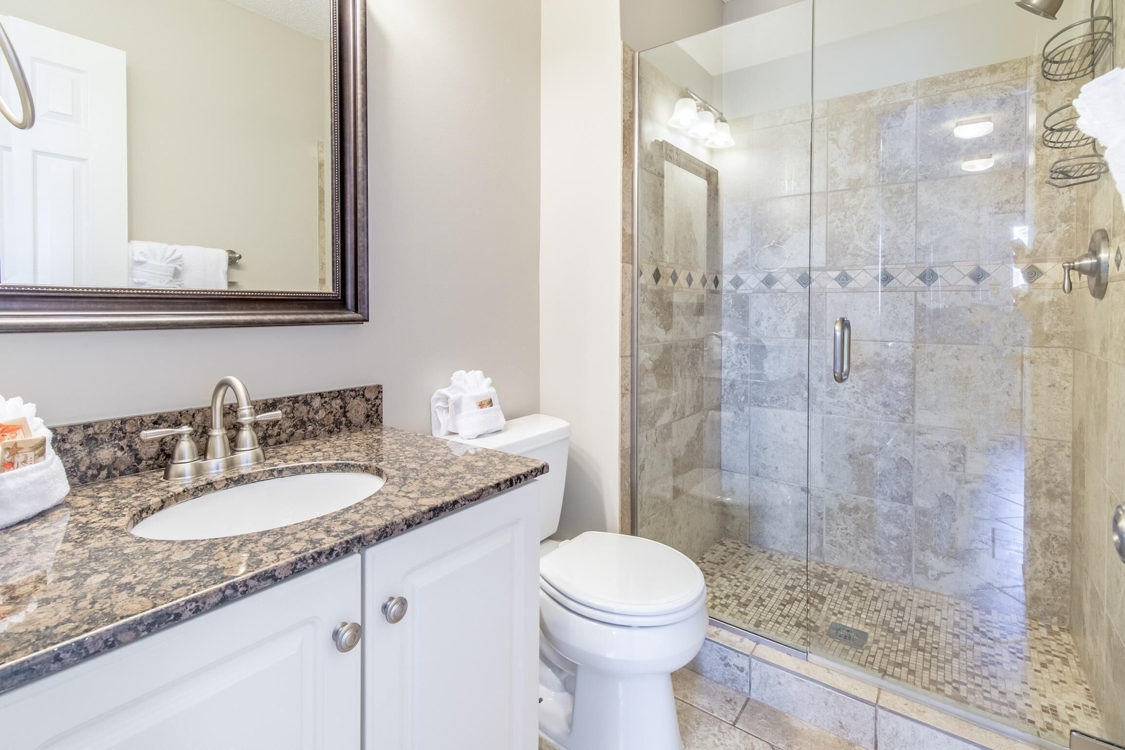 A bathroom with a granite countertop sink, a white toilet, and a glass-enclosed shower area.