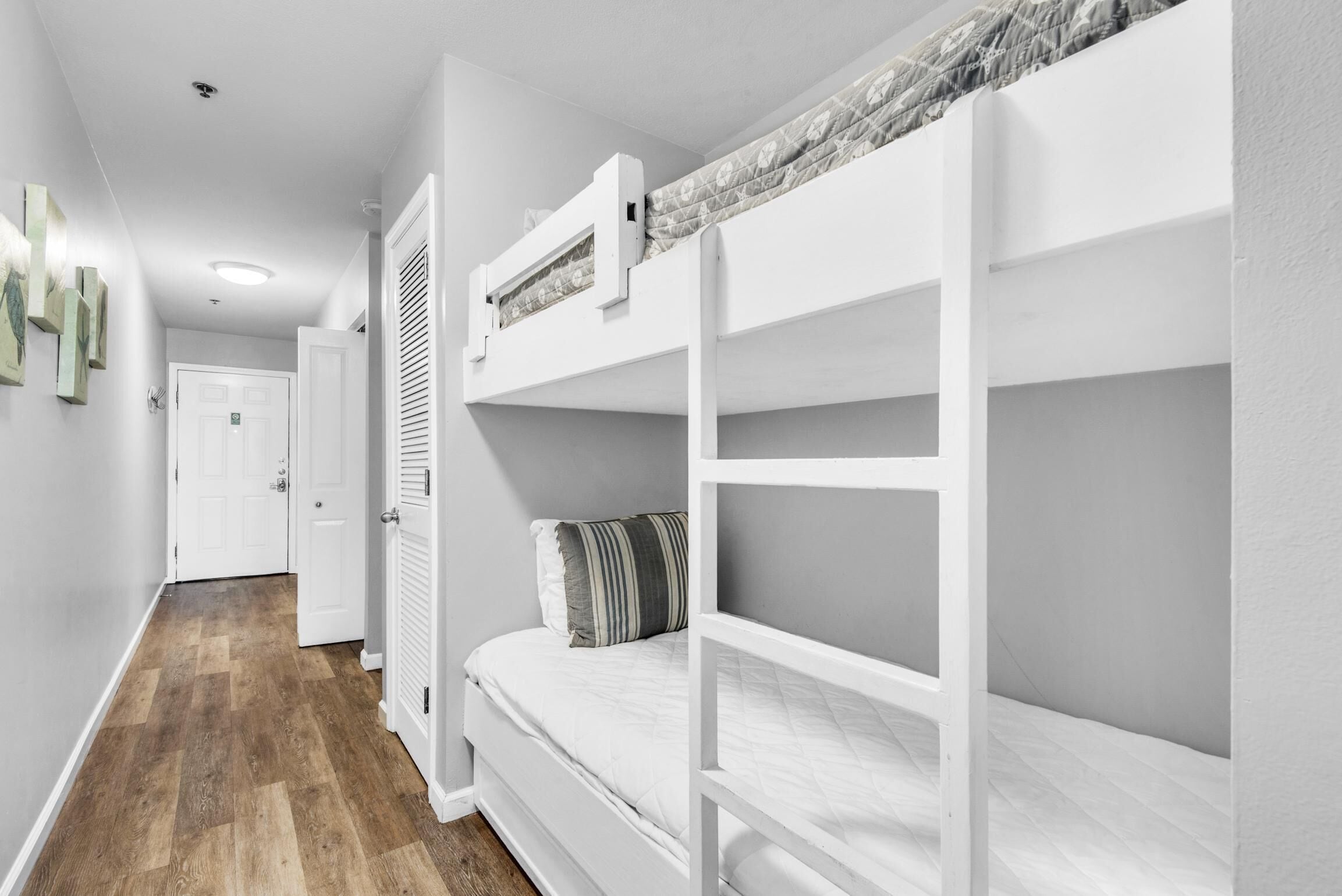 A room with bunk beds, a wooden floor, and a door leading to another room.