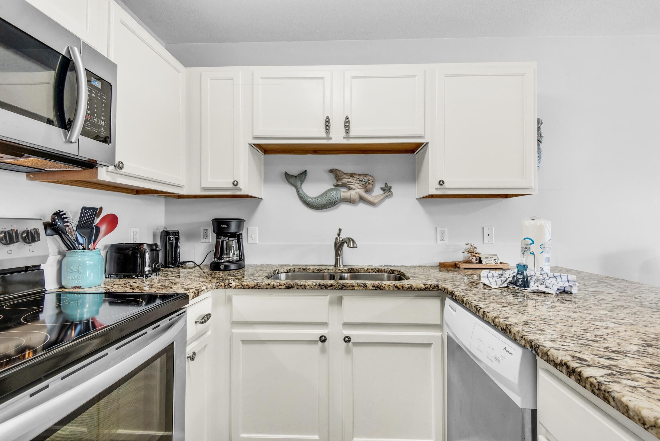 A kitchen with white cabinets, a granite countertop, a microwave, a coffee maker, and a sink.