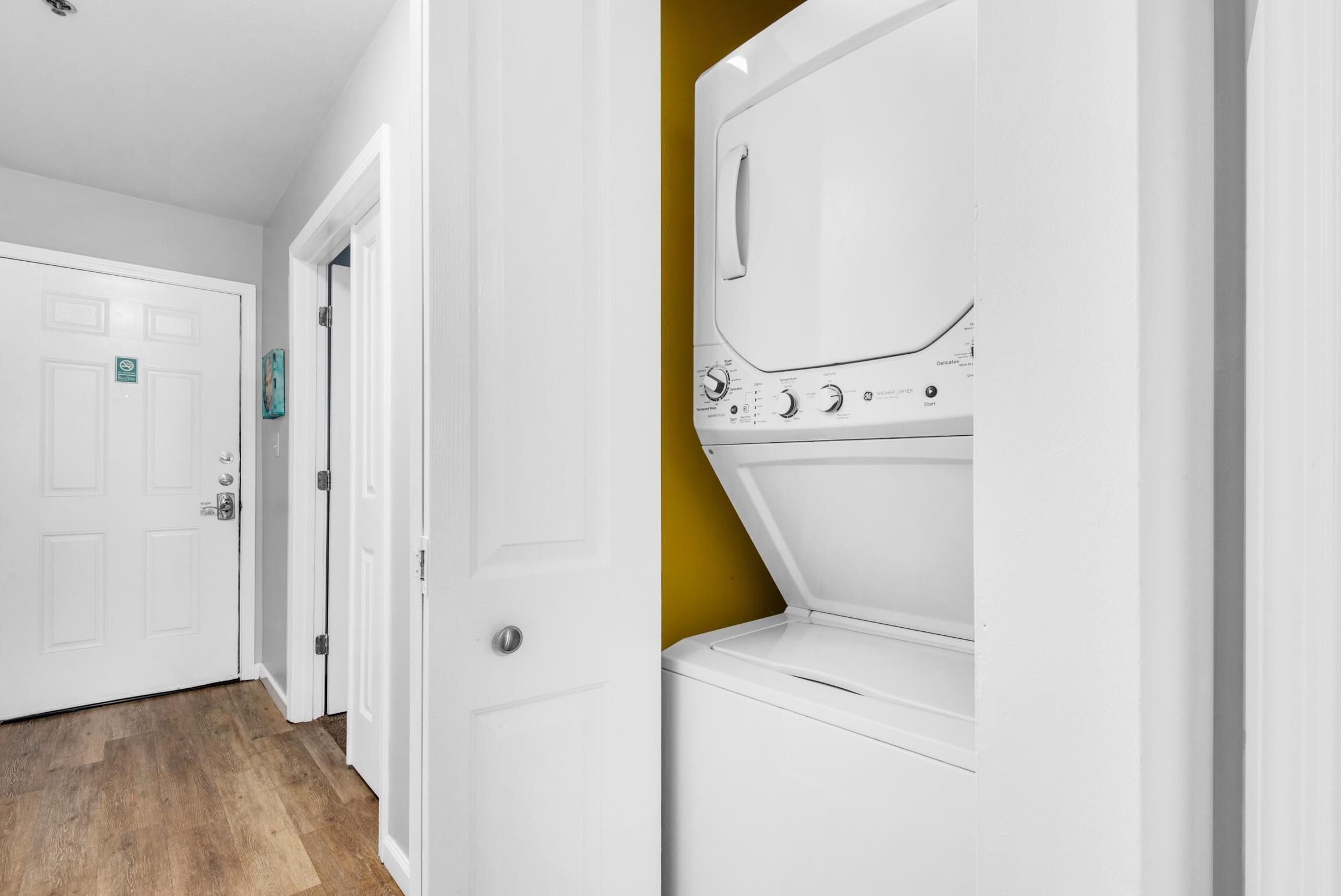 A laundry room with a white washing machine and dryer, a wooden floor, and a white door with a green sign.