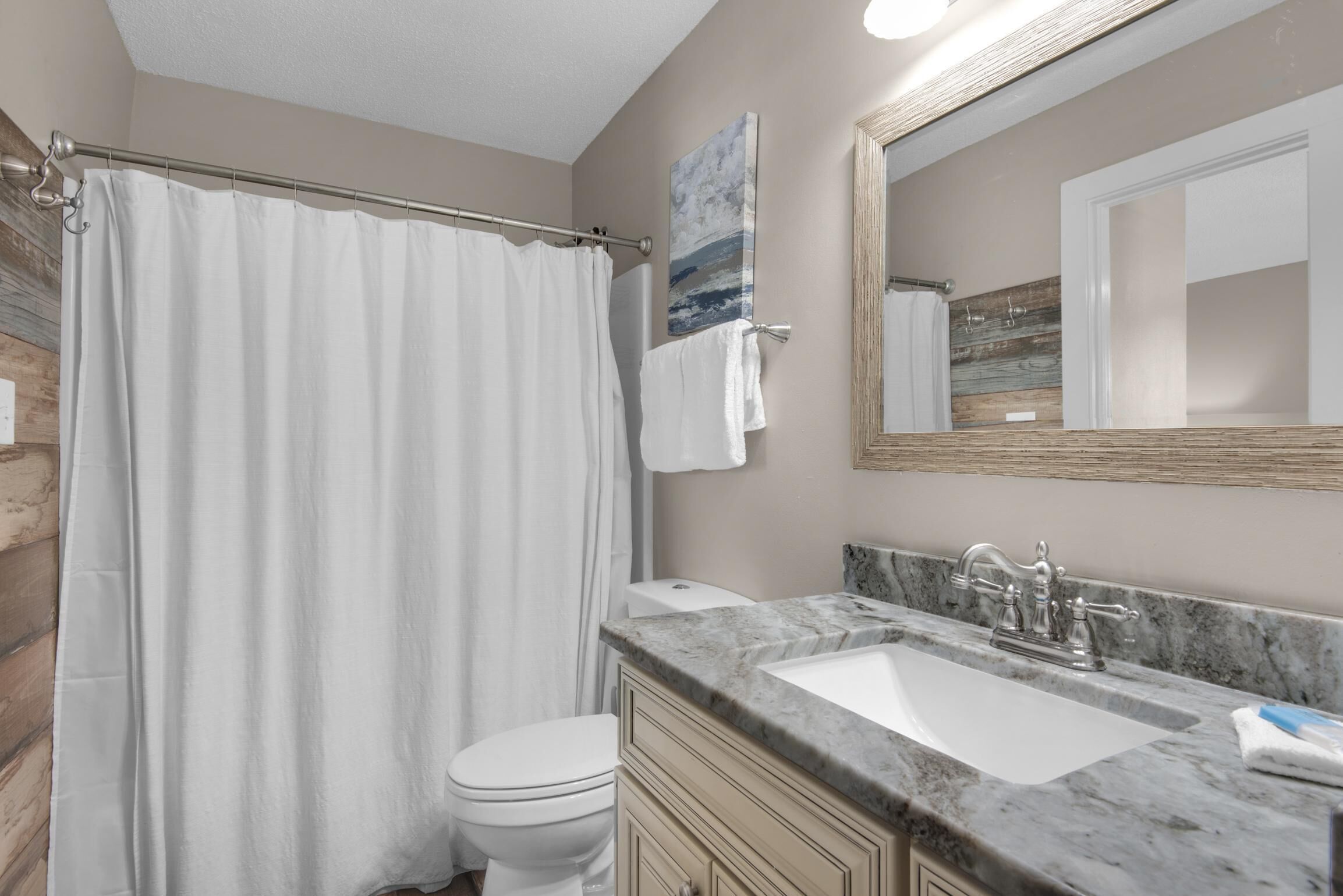 A bathroom with a shower curtain, toilet, sink, and mirror.