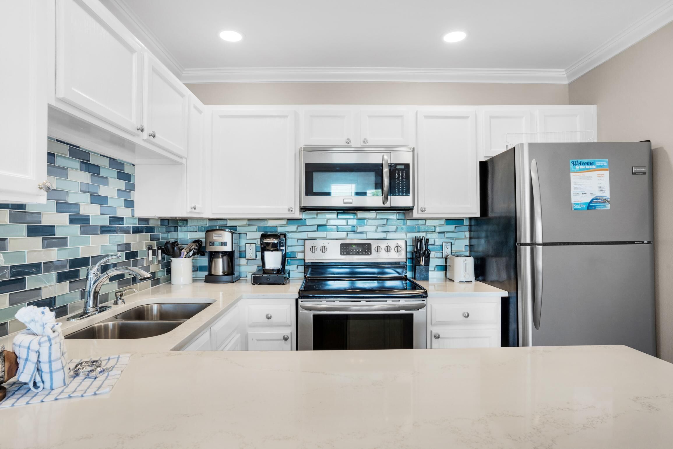 A modern kitchen with white cabinets, a stainless steel refrigerator, a microwave, a stove, and a coffee maker.