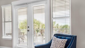 A room with a blue upholstered chair, white-framed sliding glass doors, and a view of a patio with outdoor furniture. - Grand Caribbean East 305 (Destin)