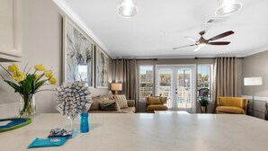 Uma sala de estar moderna com uma mesa de centro de mármore, um sofá, uma poltrona amarela e uma área de jantar com uma mesa de vidro.