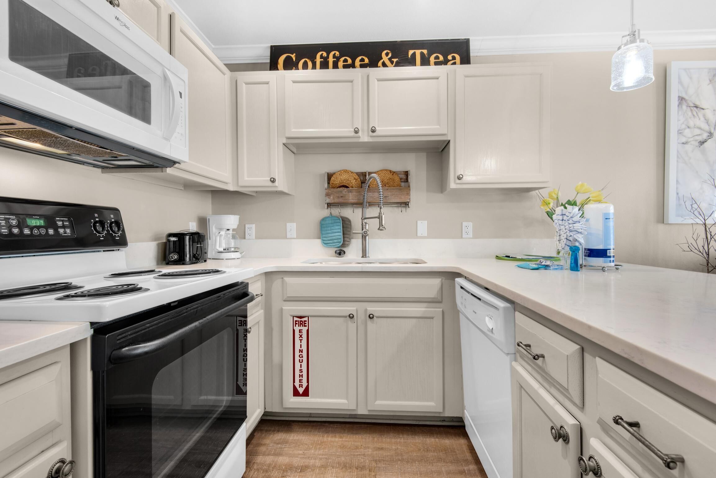 A kitchen with white cabinets, a microwave, a stove, a coffee maker, and a sign that reads "Coffee & Tea".
