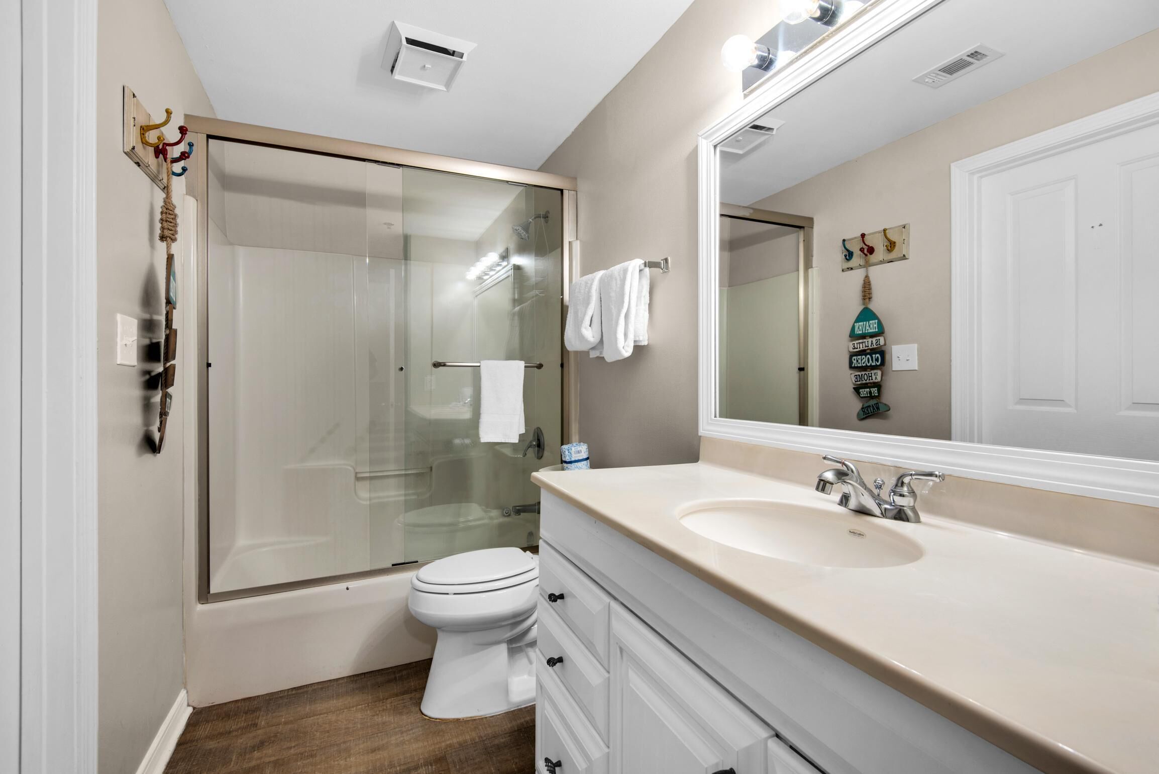 A modern bathroom with a glass-enclosed shower, a white toilet, a beige sink, and a large mirror.