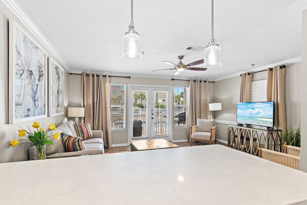 A spacious living room with a large central table, a ceiling fan, and a television.