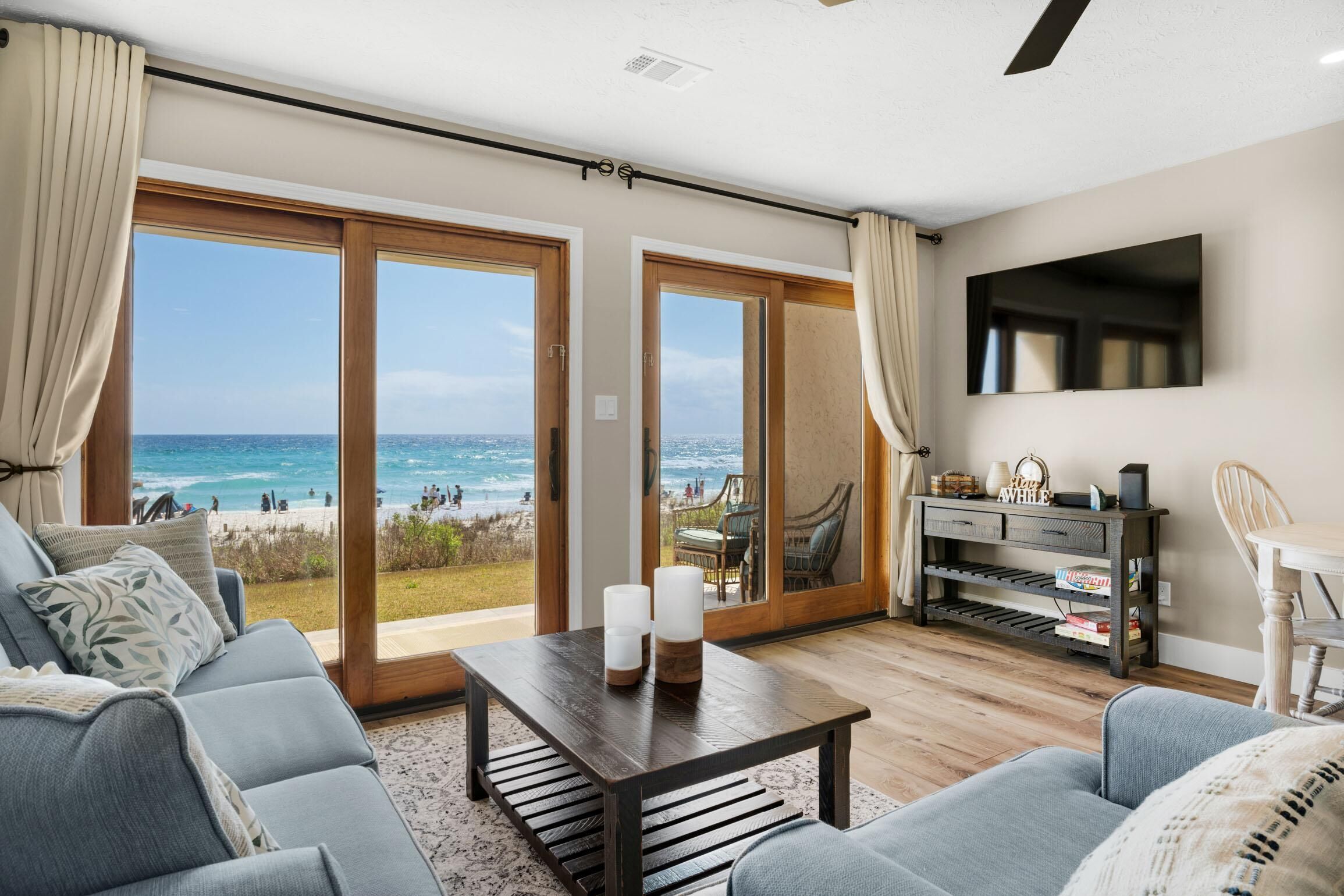 A living room with a view of the beach, a sofa, a coffee table, and a TV mounted on the wall.