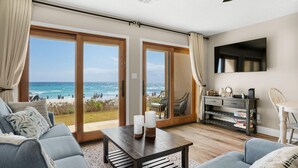 A living room with a view of the beach, a sofa, a coffee table, and a TV mounted on the wall. - Crystal Villas A-3 (Destin)