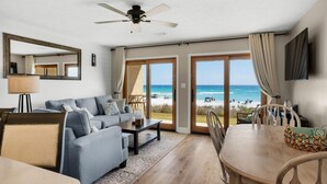 A spacious living room with a large sofa, a dining table, and a view of the beach. - Crystal Villas A-3 (Destin)