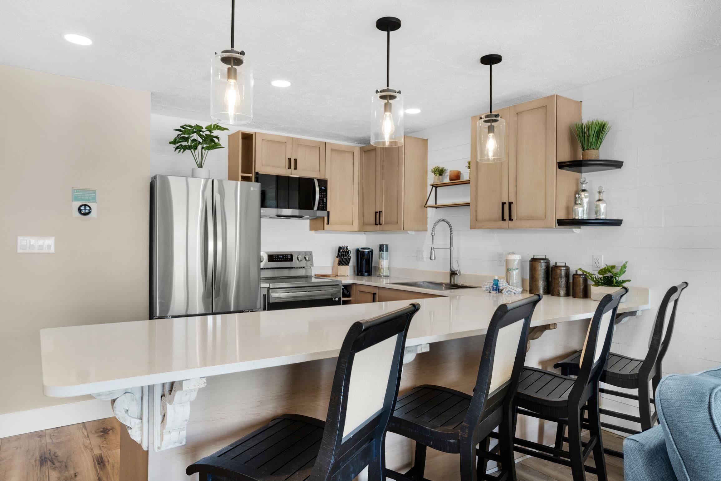 Una cocina moderna con una isla grande, electrodomésticos de acero inoxidable, armarios de madera e iluminación colgante.