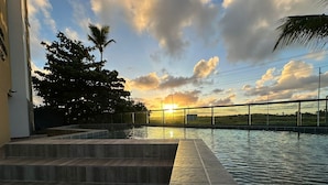 A swimming pool with steps leading into it, surrounded by trees and a sunset view. - Pousada Flor de Magnólia (Ipojuca)