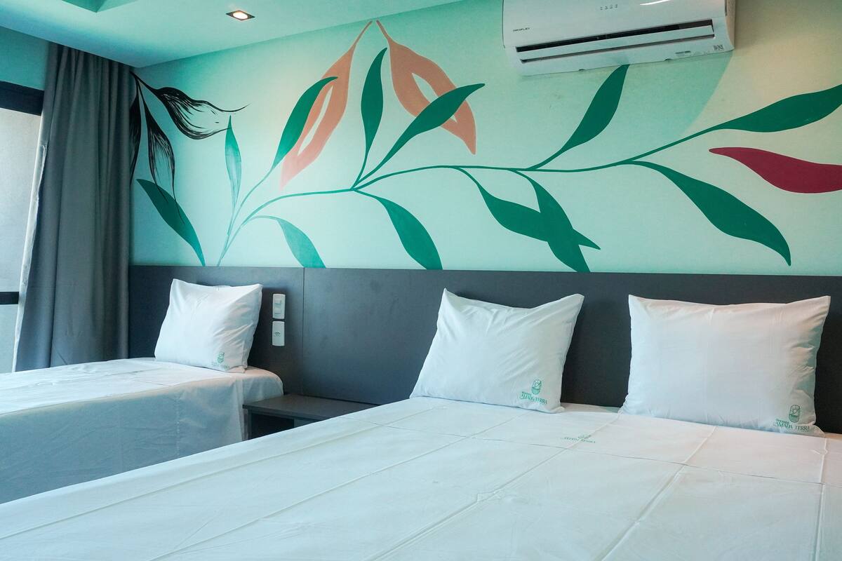 Habitación de hotel con cama, dos almohadas, cabecero, equipo de aire acondicionado y pared con diseño de hojas.