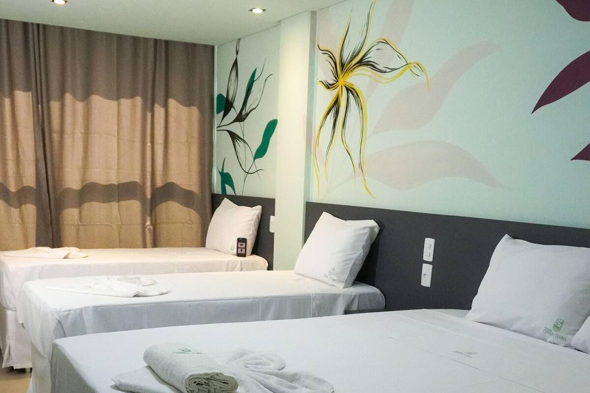 Habitación de hotel con dos camas, cada una con ropa blanca y una toalla doblada. La habitación tiene un diseño moderno con un cuadro abstracto grande en la pared y una cortina en la ventana.