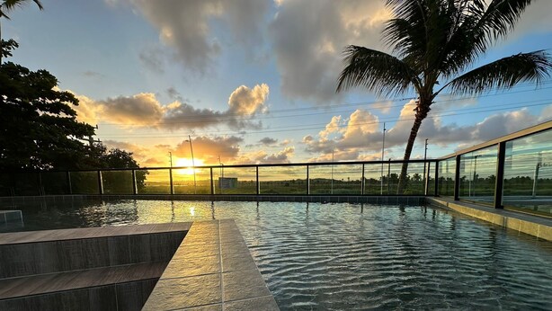 An outdoor swimming pool with a view of the sunset, palm trees, and a clear sky. - Pousada Flor de Magnólia (Ipojuca)
